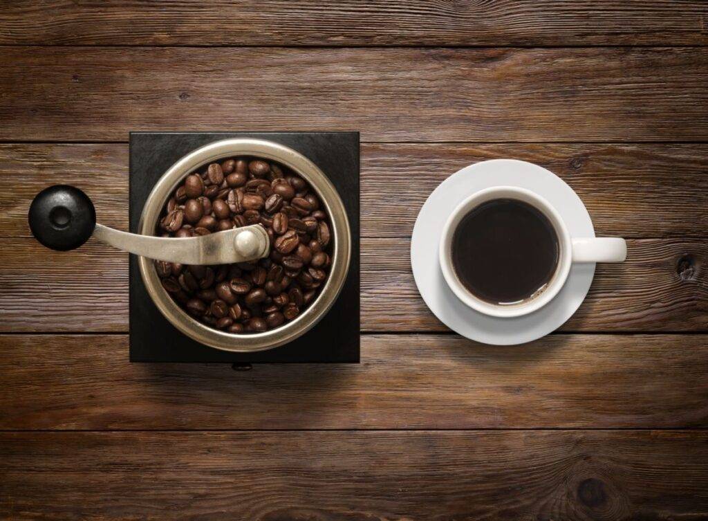 Coffee Beans in Grinder Beside Fresh Cup of Coffee